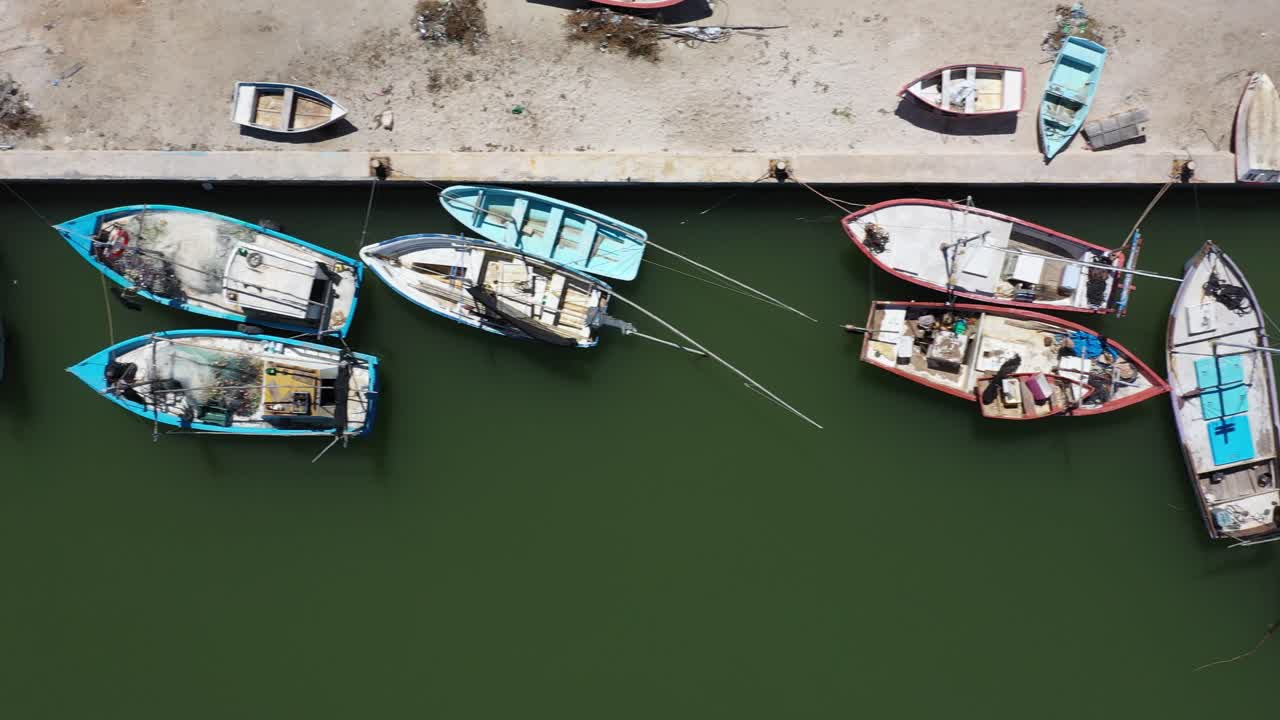 vista aérea mirando directamente hacia abajo y la cámara deslizándose hacia la derecha mostrando pequeños barcos pesqueros de madera en un puerto en méxico