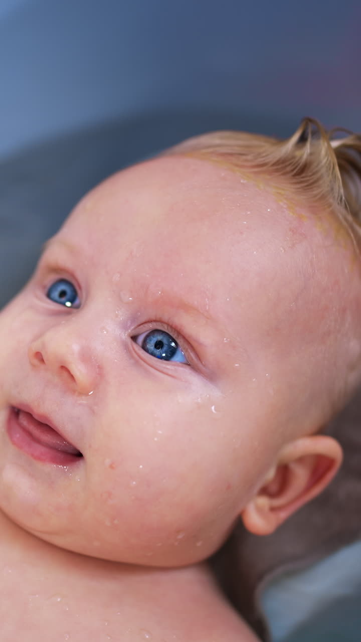 Lovely relaxed Caucasian infant baby lies in the bath tub. Cute child smiling adorably. Close up. Vertical video