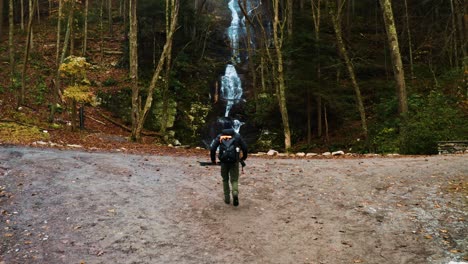 Fotógrafo-Y-Excursionista-Acercándose-A-Una-Toma-De-Un-Dron-En-Cascada