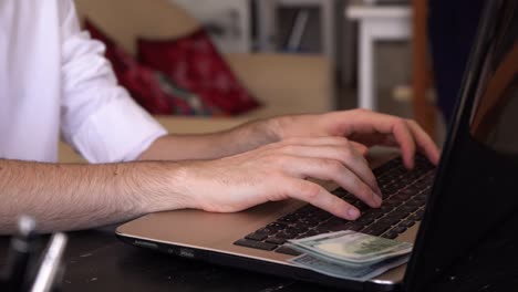 hombre trabajando y escribiendo en una computadora portátil con billetes de dólar estadounidense