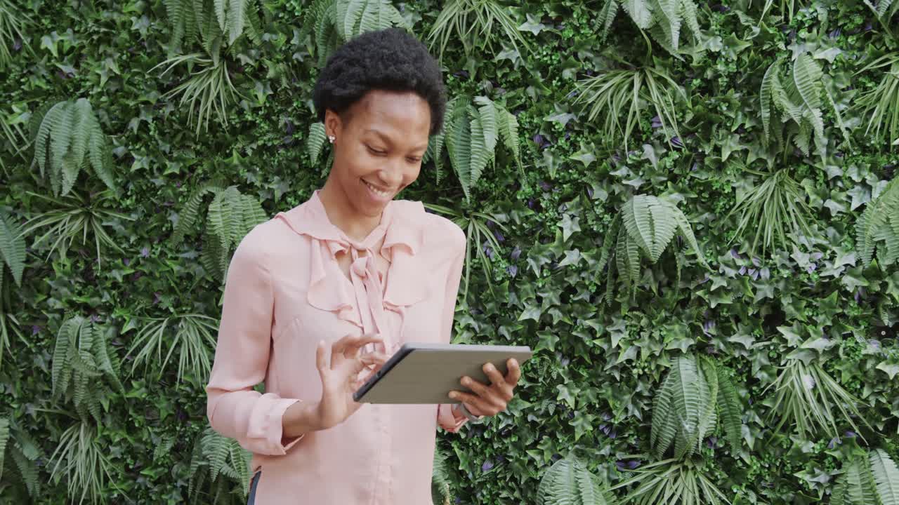 Happy african american businesswoman using tablet and smiling in garden, in slow motion