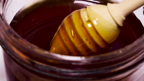 Closeup,-Wooden-Honey-Dipper-Twirling-Rich-Dark-Honey-in-Glass-Jar