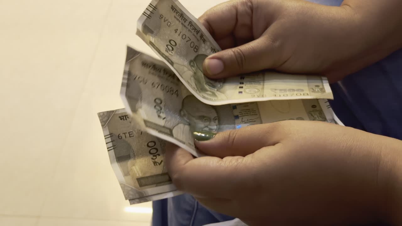 closeup of a women's hand counting an 500 rupee note of indian currency at the bank