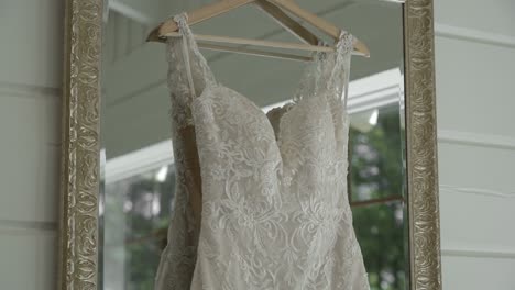 details of a beautiful white wedding gown hanging in a mirror in a well lit sunny white room