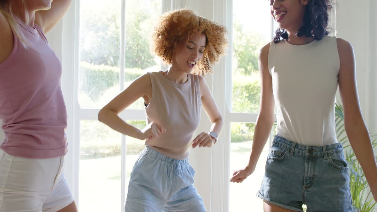 Dancing three women swaying and punching at home by glass doors, wearing summer clothes, wristwatch