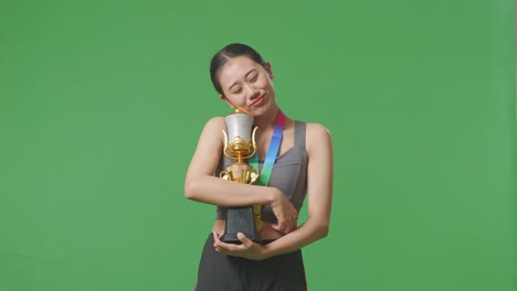 asian woman with a gold medal hugging a gold trophy being proud winning as the first winner on green screen background in the studio