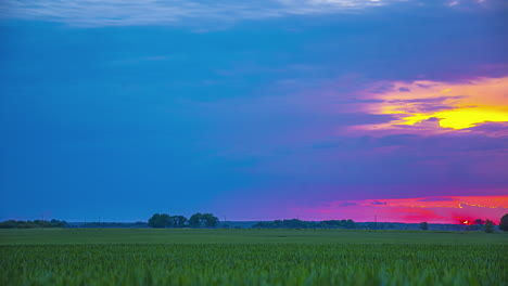 Timelapse-of-a-colorful-sunset-over-a-field,-the-sun-hidden-behind-the-clouds