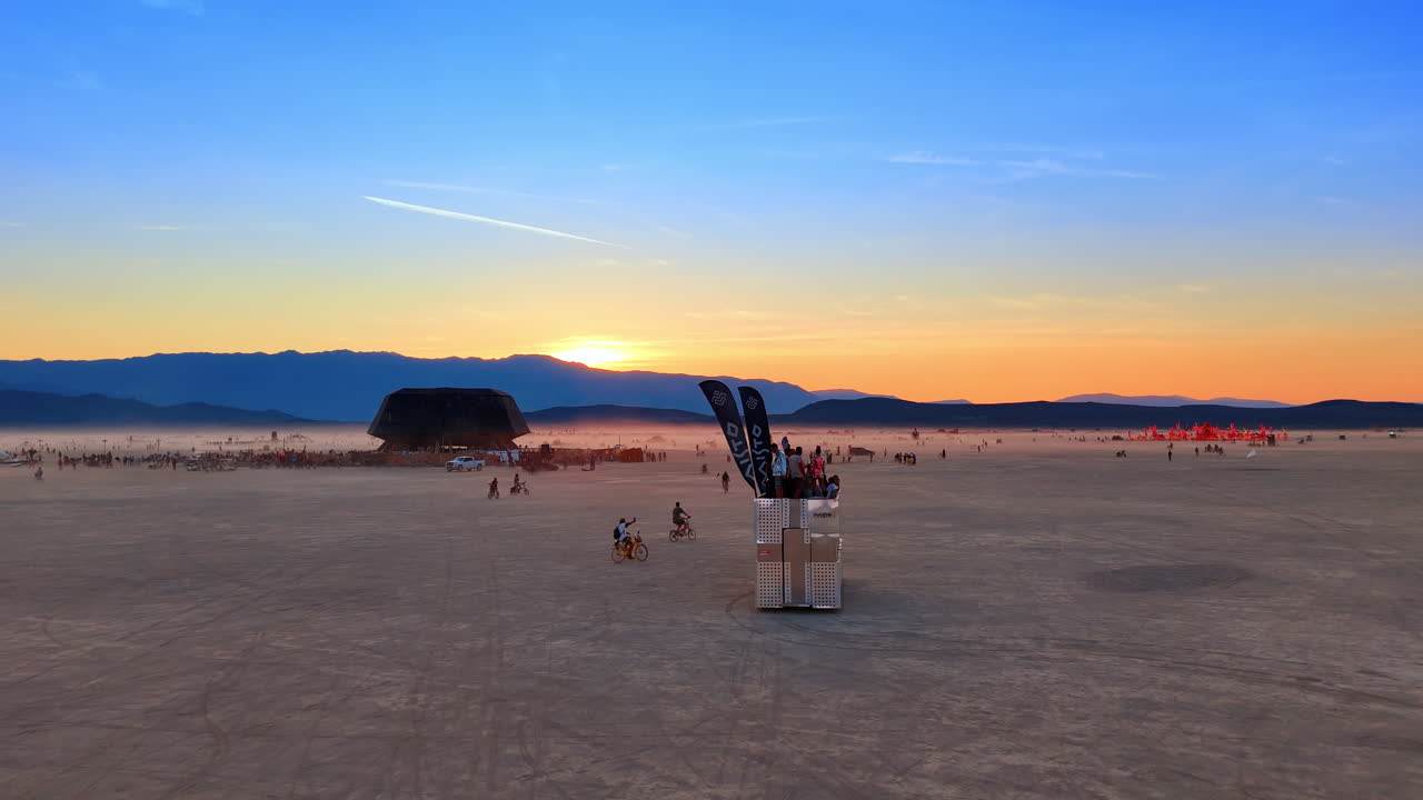 California, USA, 1 July 2025: Mobile sound stage moving across desert during sunset. Side view of a metallic mobile unit with people on top driving through a vast dusty plain under a colorful sky