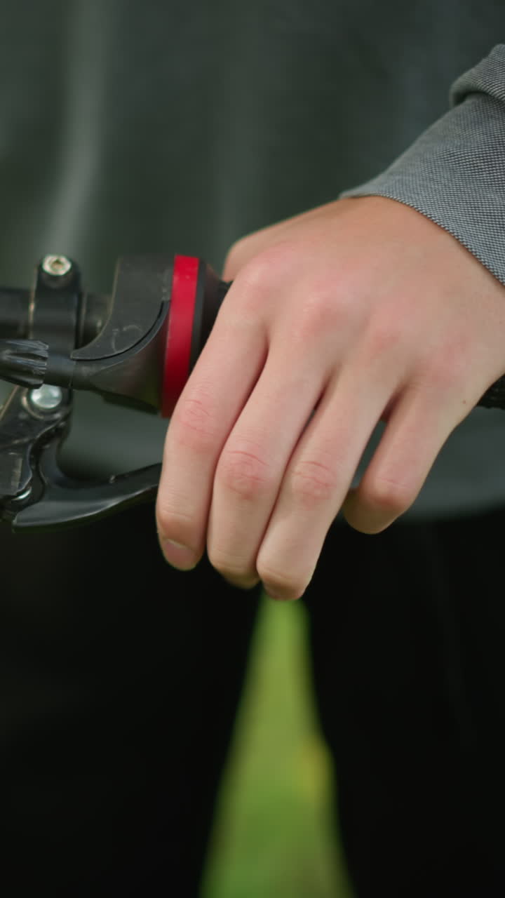 잔디에 주차된 자전거의 손잡이를 조정하는 누군가의 클로즈업, 사람이 튼튼한 손잡이로 손잡을을 잡고, 주차장에 서서 브레이크 기능을 확인합니다.