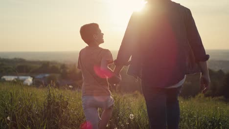 little boy walking with dad at the meadow during the sunset.