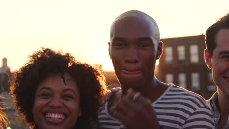 Friends-at-a-rooftop-party-smiling-to-camera,-handheld-pan