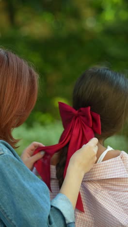 woman helping a girl with a red bow