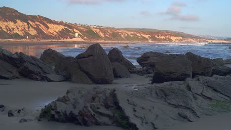 Corona-Del-Mar-Beach-with-a-close-up-view-of-the-rocks-with-cliffs-and-small-waves-of-the-pacific-ocean-in-the-back