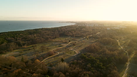 parque natural de sobrevuelo aéreo lento con árboles y senderos para caminar durante el amanecer - tranquilo mar batlic ighting en el telón de fondo - polonia, europa