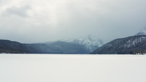 Niedrige-Winterantenne-über-Einem-Zugefrorenen-See-Mit-Großen-Bergen-Im-Hintergrund