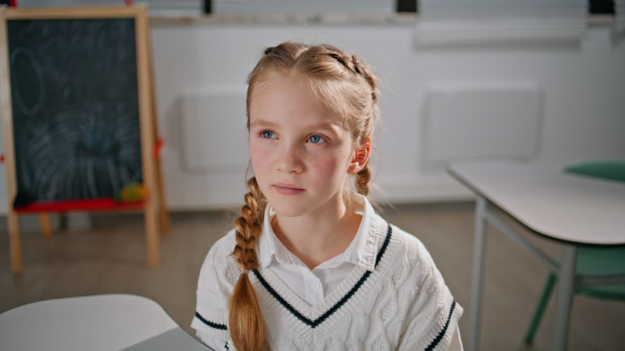 Smart schoolgirl raising hand answering classroom portrait. Girl looking camera