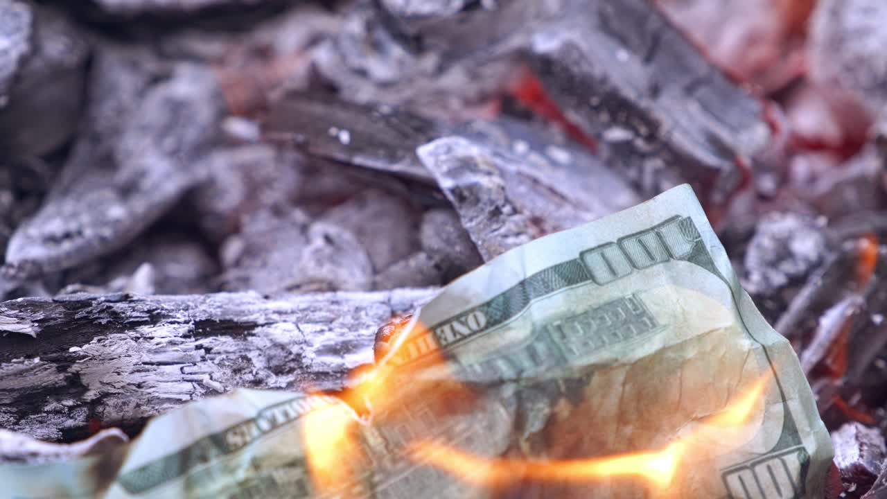 Crumpled dollar banknote burning on fire. Burning up firewood and hand throwing one hundred dollar bill into the fire. Burning money. Close-up.