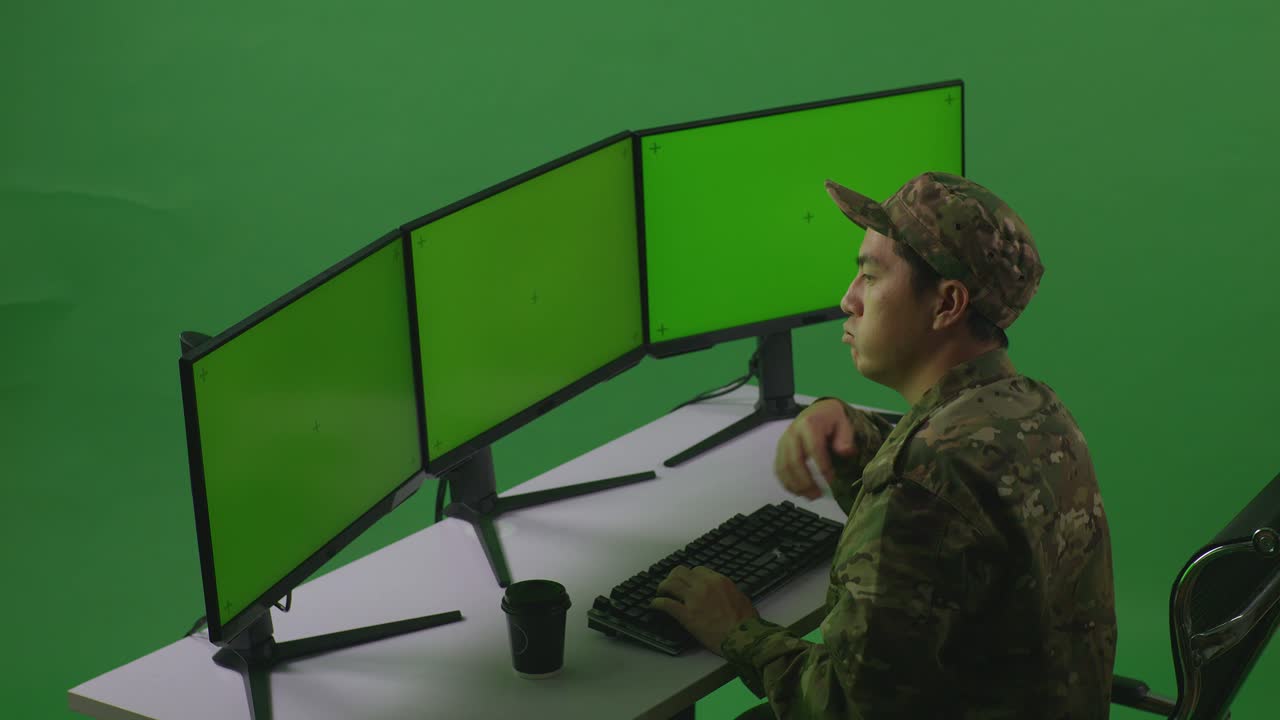 vista laterale di un uomo asiatico annoiato soldato che lavora con un simulacro di più monitor di computer in uno studio a schermo verde