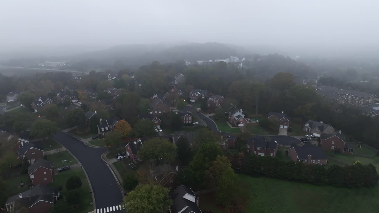 Drone footage circling over a large neighborhood in the morning on a foggy day in the fall.