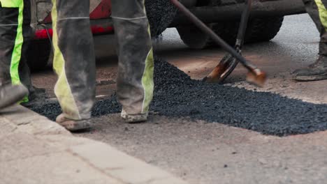 construction workers are spreading new asphalt onto broken patch of road