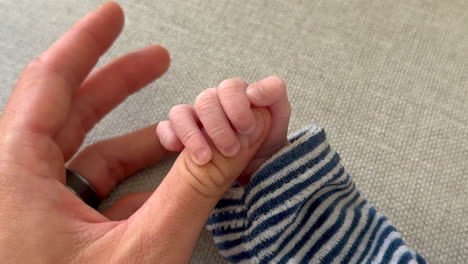 primer plano de la mano del bebé recién nacido sosteniendo el dedo pulgar de un adulto en casa