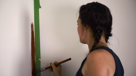 young woman paints red wall in house