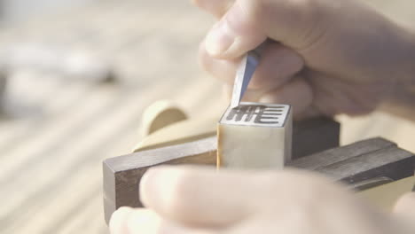 close up shot of hands and tool carving chinese name ma on traditional chop stamp