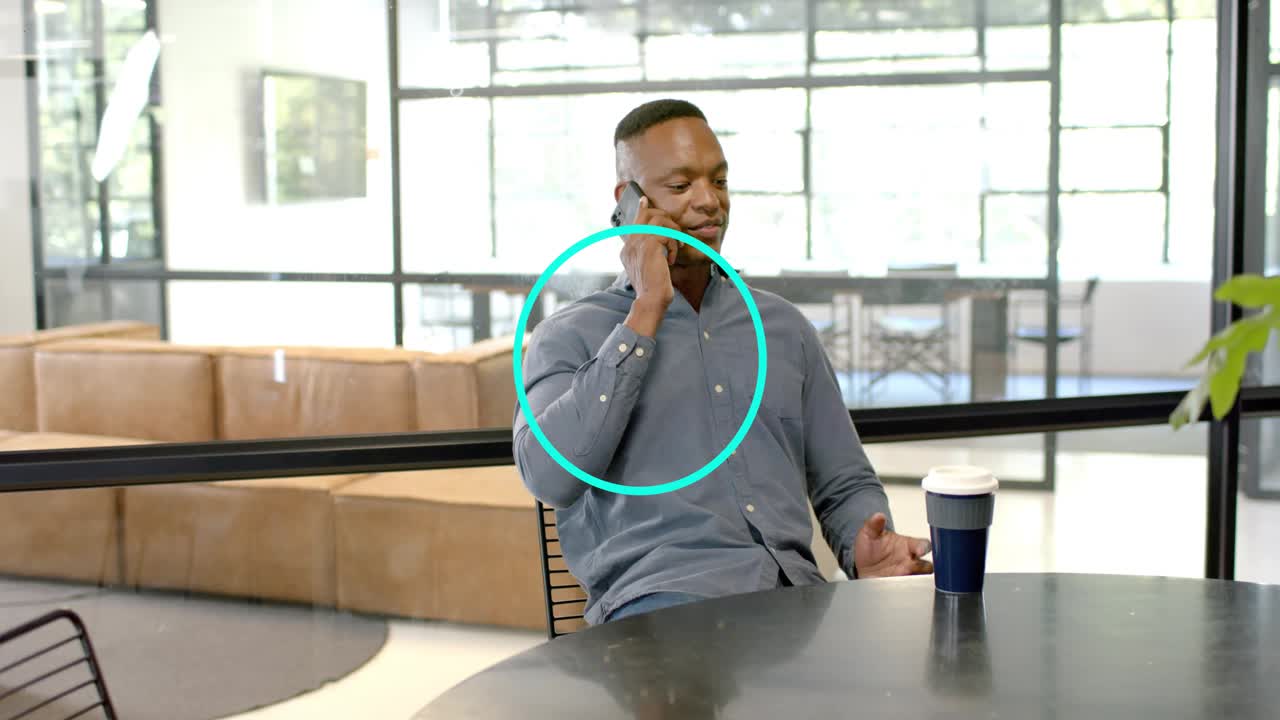 Man on phone making work call talking leaning back smiling reaching cup blue dot overlay shifting