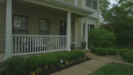 Front-of-a-small-new-house-in-the-suburbs-with-a-woman-sitting-on-a-couch-on-the-front-porch