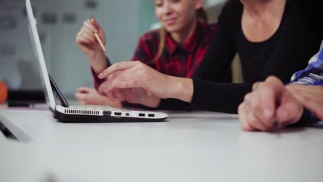 closeup view of hands of creative business team of three people working at the laptop in a modern office. they are discussing business ideas while looking at the screen and typing