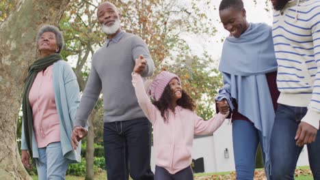 video of happy african american parents and grandparents walking with granddaughter in garden