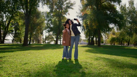 smiling mother holding phone turning making selfie video in sunny spring park.