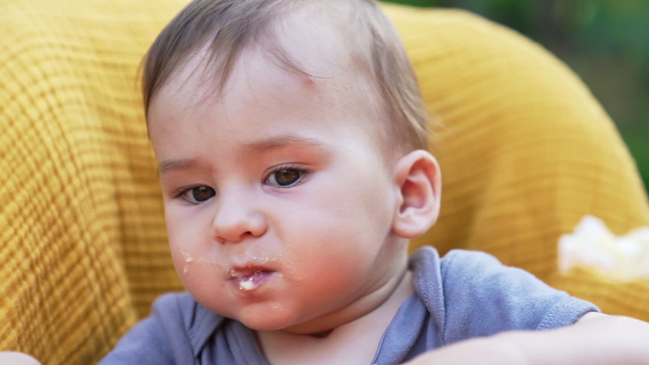 Adorable baby with porridge on his face refuses to eat. Portrait of a child being fed from a spoon. Close up.