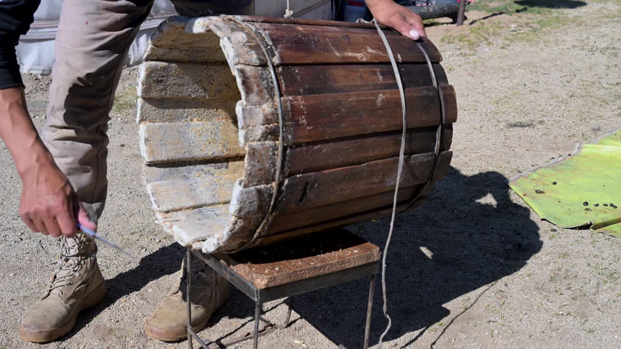 Man assembling a drum on a stool outdoors