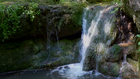 Rising-close-up-shot-of-flowing-waterfall-down-mossy-rocks-with-alp-mountains-of-Austria