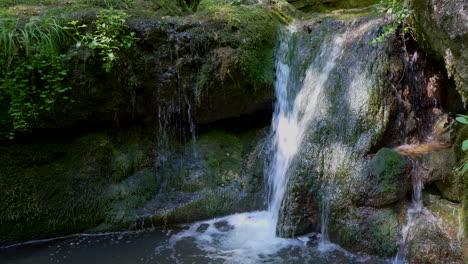 levantamiento de cerca de la caída de agua que fluye por las rocas de musgo con las montañas alpinas de austria