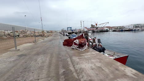 -Close-up-shot-over-fishing-net-beside-fishing-motor-boats-docked-along-the-seaside-on-a-cloudy-day