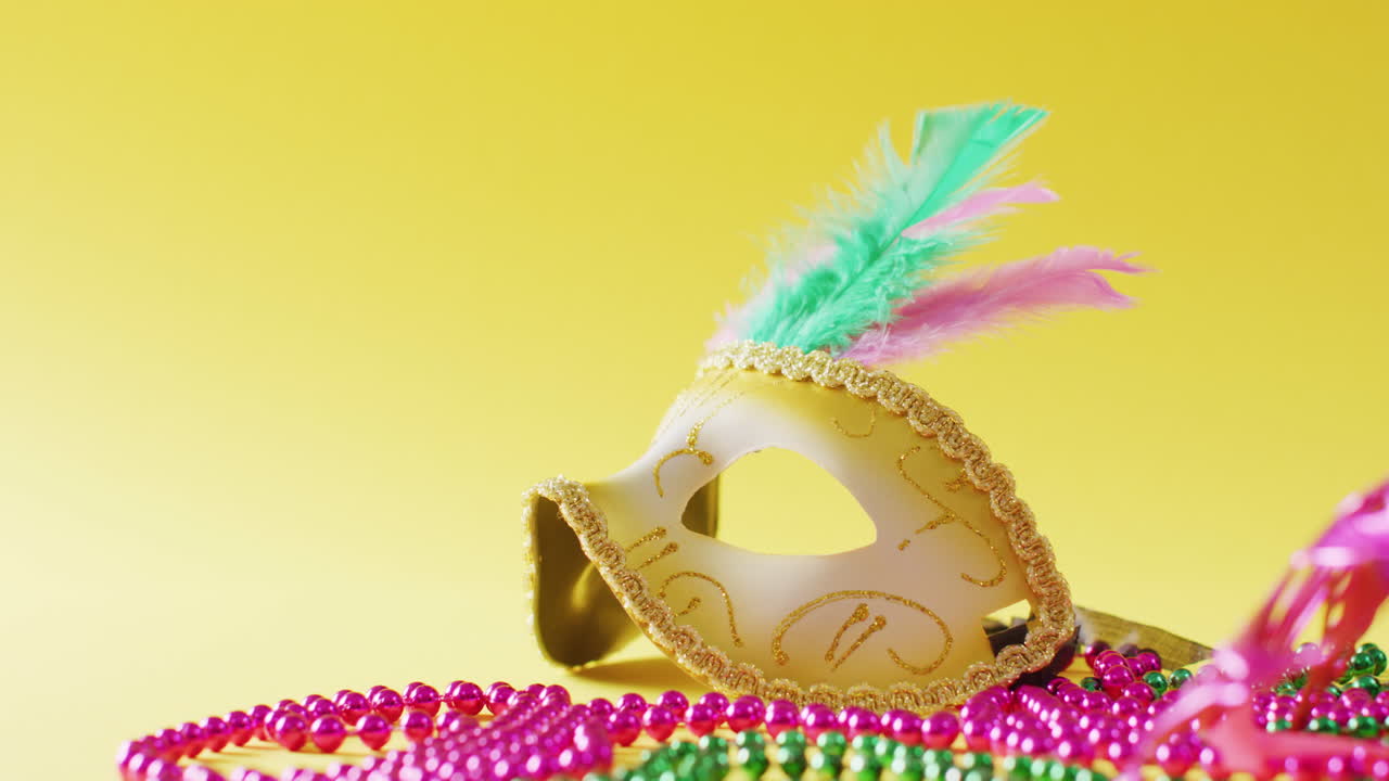 Video of masquerade mask with feathers and mardi gras beads on yellow background with copy space