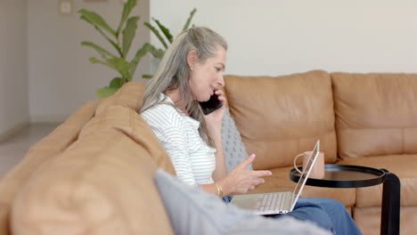 Mujer-Caucásica-Hablando-Por-Teléfono,-Mirando-El-Portátil-En-La-Sala-De-Estar