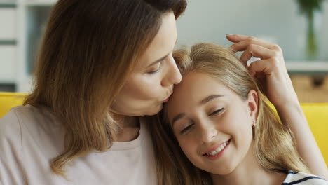 close up view of woman hugging her cute teen daughter while they sitting on couch and watching something on laptop in living room