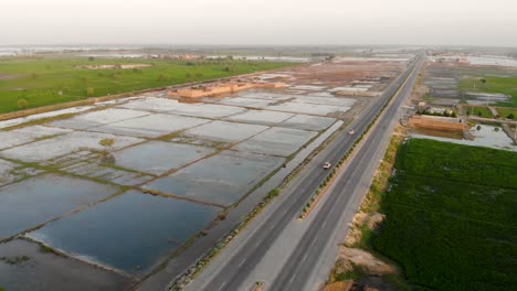 Luftaufnahme-Der-Autobahn,-Die-Durch-Das-Ländliche-Jacobabad-Führt,-Mit-Wasserfeldern-Auf-Der-Linken-Seite