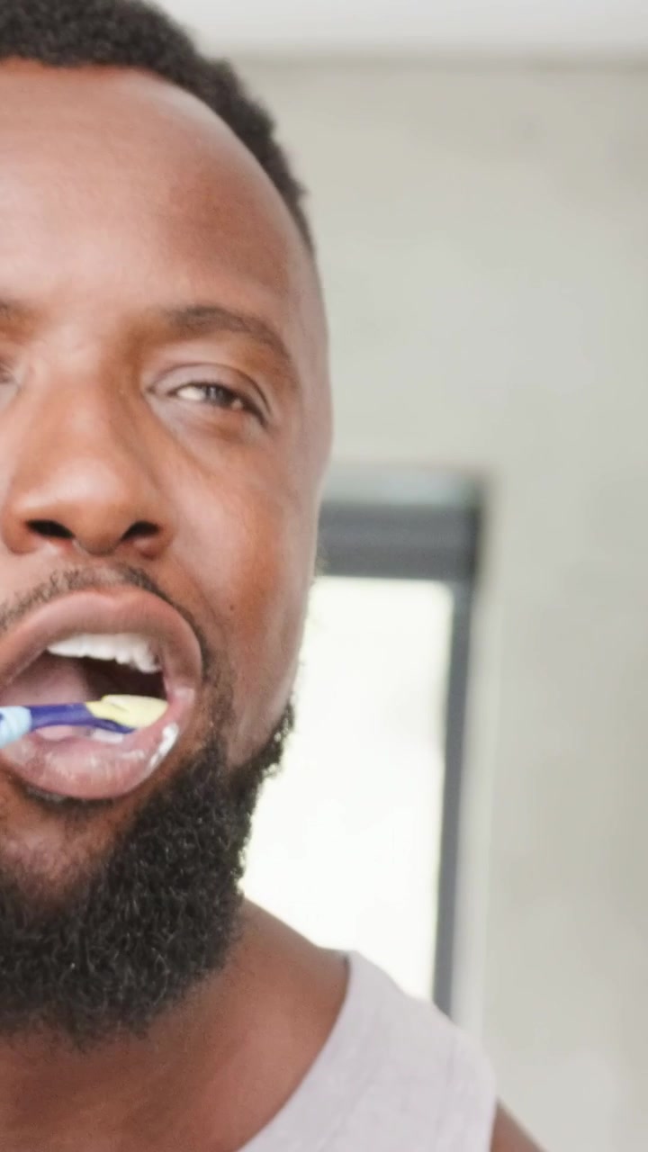 Vertical video: Brush entering, man in gray tank brushing teeth for hygiene in bathroom, copy space