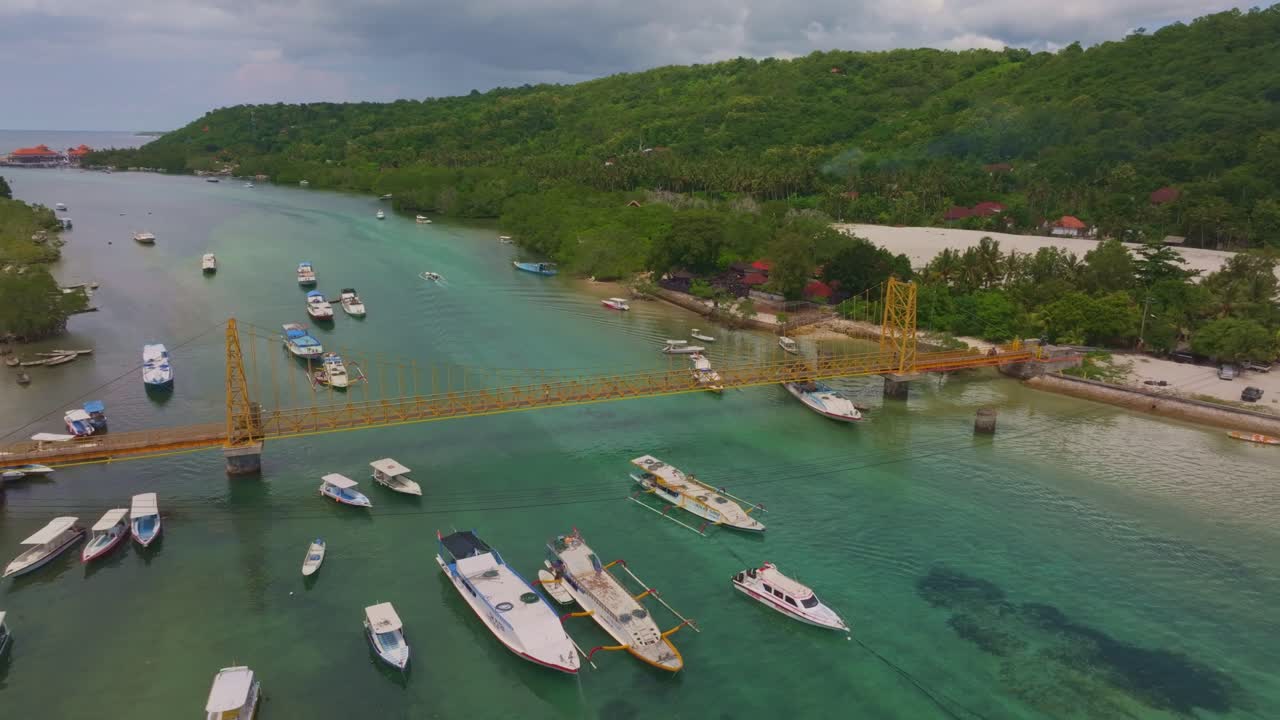 Vista aerea del bellissimo ponte giallo che collega le isole sull'oceano nella zona di Nusa Ceningan, con scooter che attraversano e barche ancorate nel paesaggio tropicale di Bali
