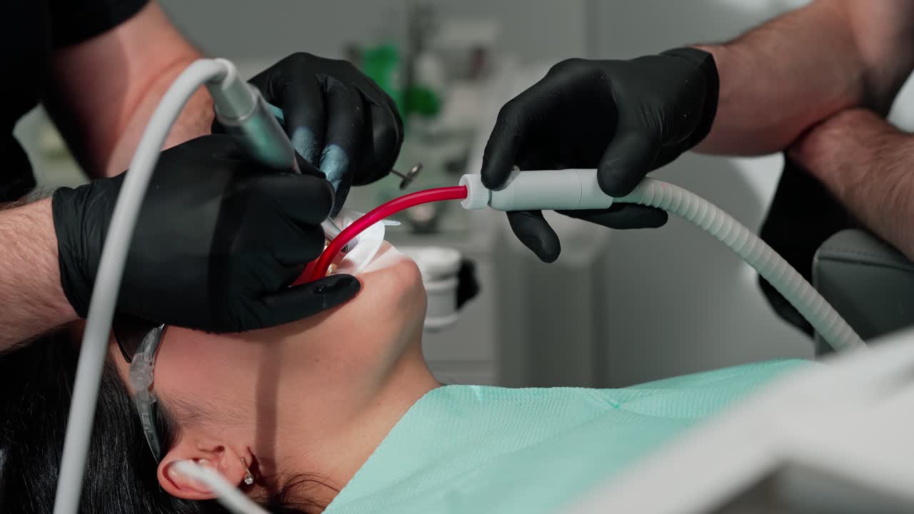 Dentist's hands in black gloves treating woman's teeth. Stomatologist with assistant use modern methods to treat client's tooth. Close-up.