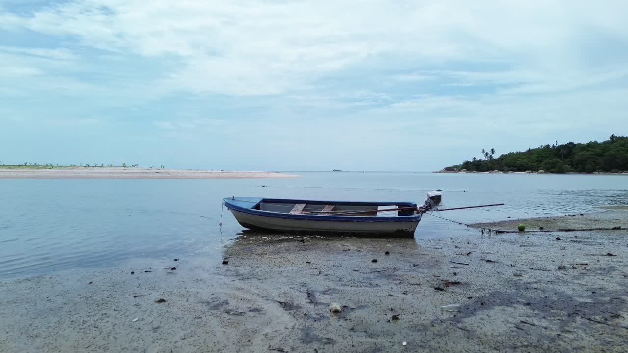 Drone video shows traditional small fishing boats anchored near the sandy shoreline of Koh Phangan, Thailand, with clear turquoise water and lush green coastline creating a scenic tropical seascape