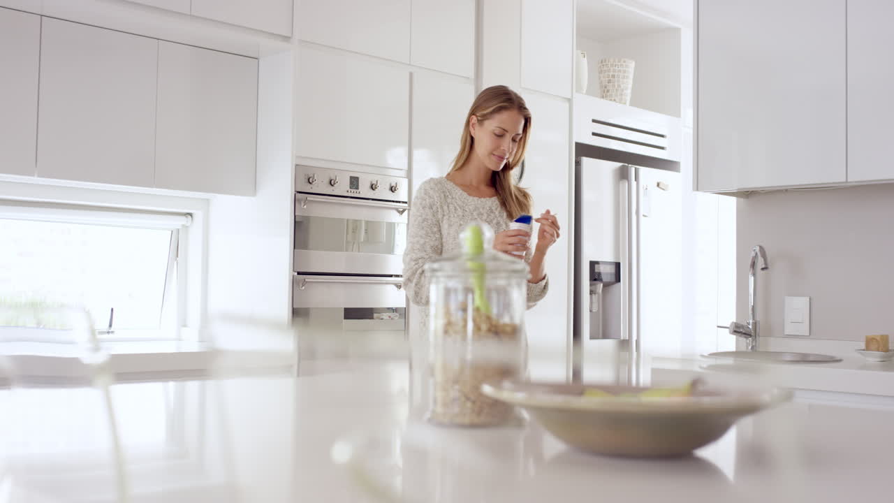 Donna che mangia yogurt naturale nella cucina di una lussuosa casa bianca e immacolata