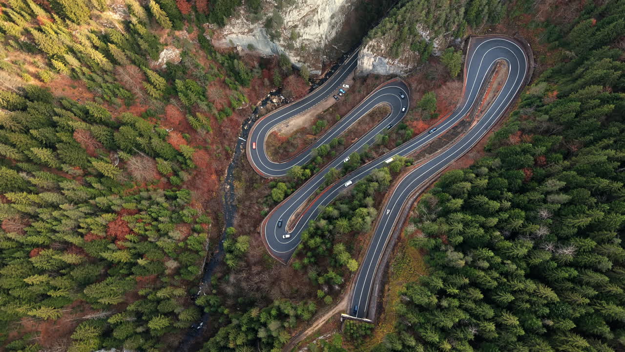 Aerial drone view of nature in Romania. Carpathian mountains, serpentine road with cars in the valley, rocky hills covered with lush forest