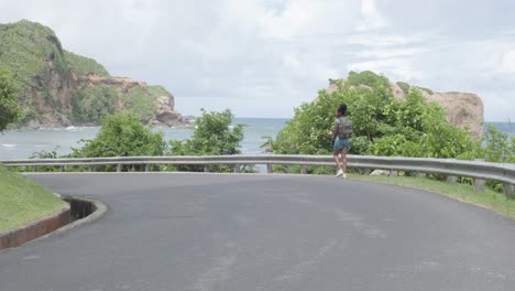 woman in dress walks along an ocean view road in calibishie dominica