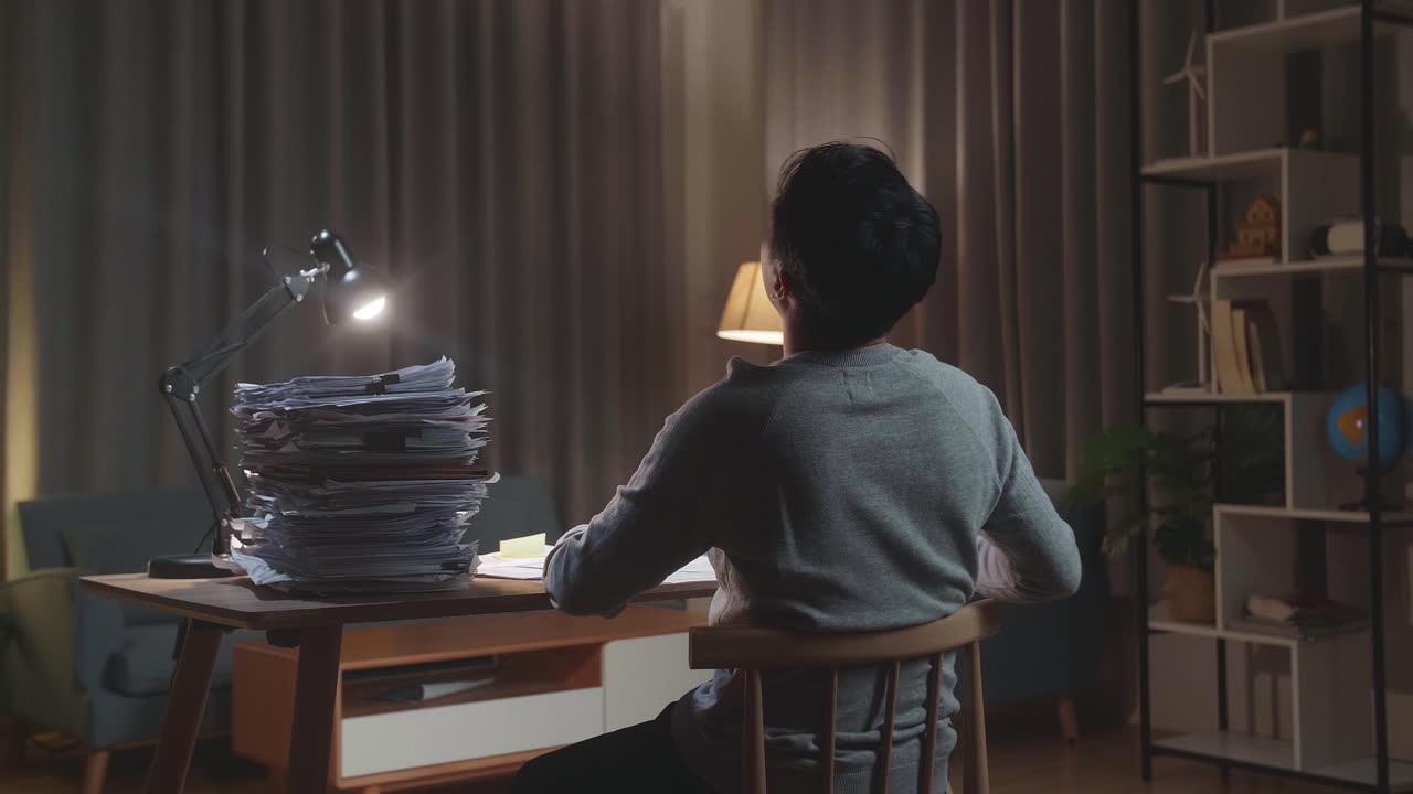 지친 아시아인 남자가 집 의자에 기대어 서류로 열심히 일하면서 잠을 자고 있는 모습