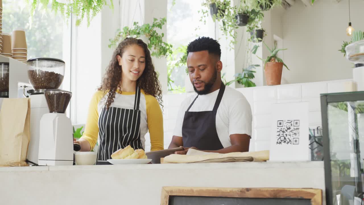 feliz dueño de un café afroamericano y barista biracial usando una tableta en el café
